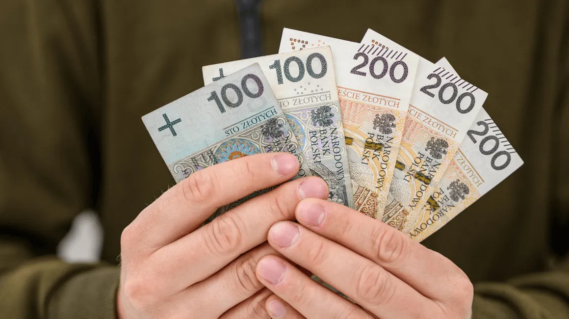 Człowiek trzyma w dłoniach banknoty 100 i 200 zł